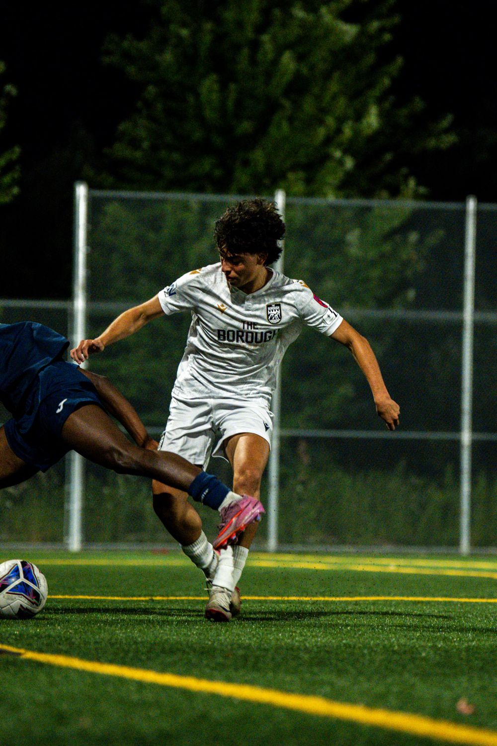 Player in white kit cutting past a diving defender under floodlights